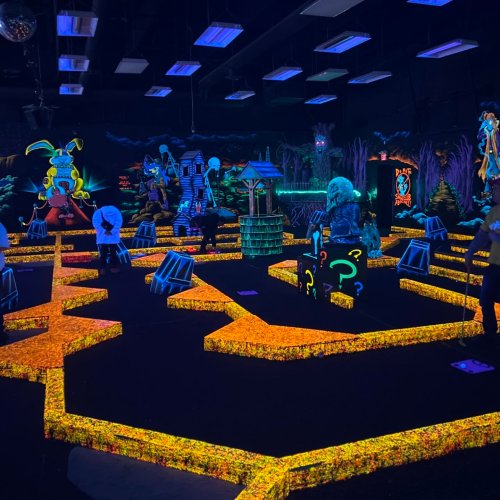 A vibrant glow-in-the-dark mini-golf course with colorful obstacles and neon decorations in a darkened room.