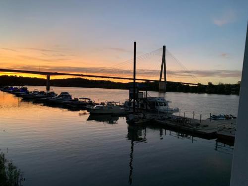 Sunset over a calm river with boats docked and a cable-stayed bridge in the background.