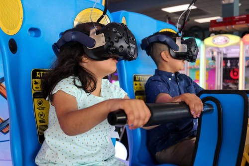 Two children wearing virtual reality headsets sit in gaming chairs, focused on their immersive experience.