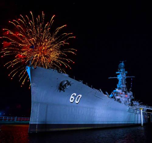 A battleship illuminated at night with colorful fireworks exploding in the background.