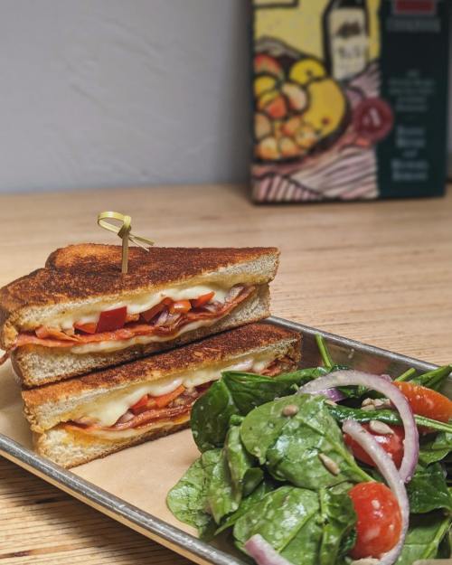 A toasted sandwich with cheese, tomatoes, and onions, served with a side of fresh spinach salad.