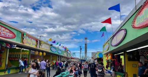 A lively fairground scene with colorful stalls, flags, and people enjoying the festivities under a cloudy sky.