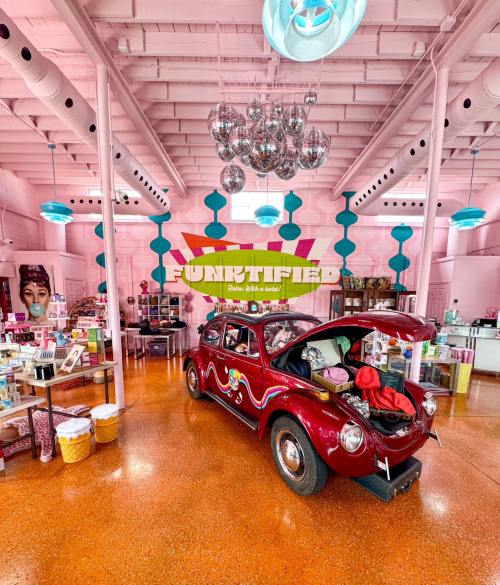 A vintage red car with an open trunk inside a colorful, retro-themed shop filled with beauty products and decor.