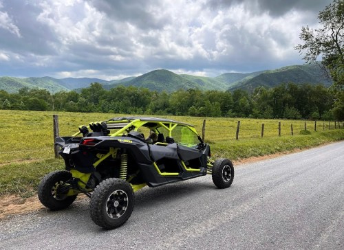 A black and yellow off-road vehicle parked on a gravel road, with mountains and cloudy skies in the background.