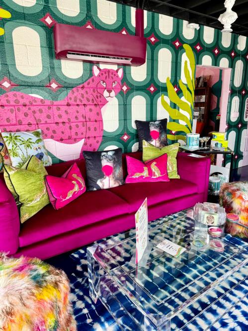 A vibrant lounge with a pink sofa, colorful pillows, and a bold leopard mural on the wall. Bright and eclectic decor.