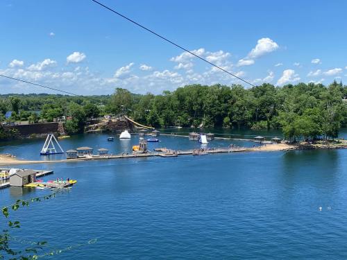 A scenic view of a lake with sandy beaches, water activities, and lush greenery under a blue sky with fluffy clouds.