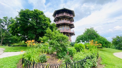 A wooden observation tower surrounded by lush greenery and colorful flowers under a cloudy sky.