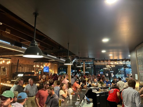 A crowded bar scene with people socializing, dim lighting, and a lively atmosphere.