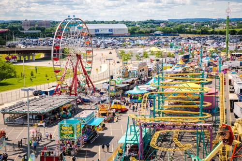 A vibrant carnival scene featuring a Ferris wheel, rides, and colorful booths under a blue sky.