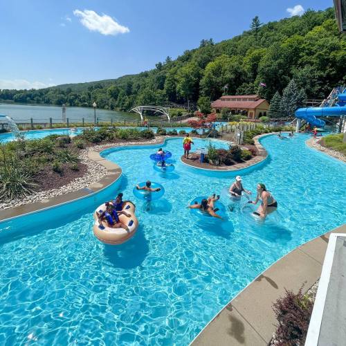 A sunny water park scene with people floating on tubes and enjoying the lazy river, surrounded by greenery.