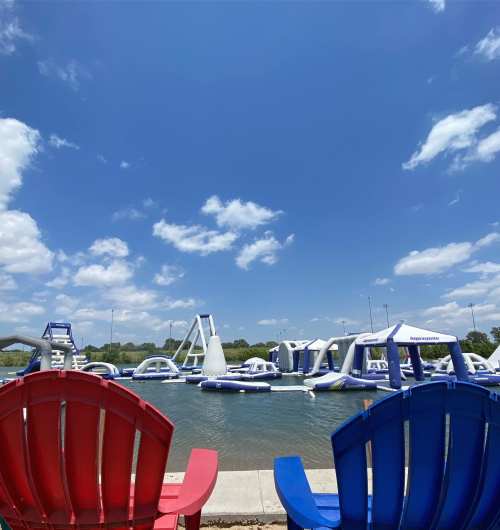 Colorful adirondack chairs by a water park with inflatable attractions under a clear blue sky.