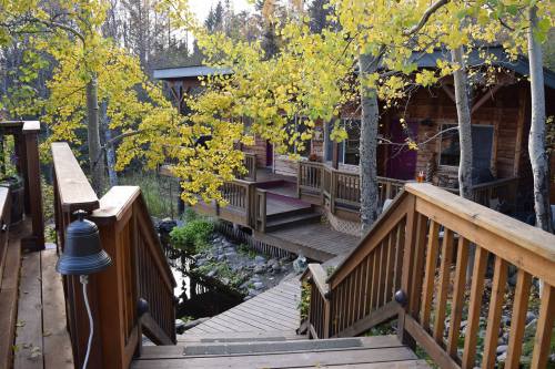 A wooden staircase leads down to a cozy cabin surrounded by autumn trees and a small pond.