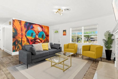 A stylish living room featuring a colorful mural, gray sofa, yellow chairs, and a glass coffee table.