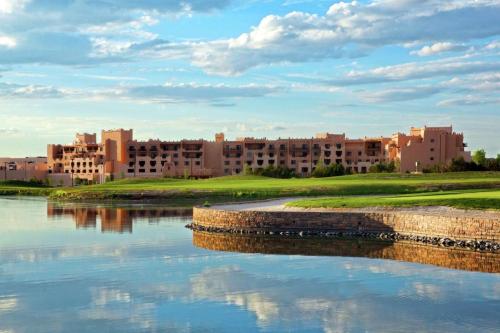 A serene landscape featuring a hotel by a lake, with lush green grass and a cloudy blue sky reflecting in the water.