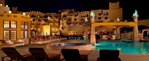 A luxurious resort pool area at night, featuring lounge chairs, a hot tub, and illuminated architecture.