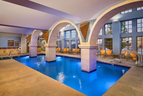 Indoor swimming pool with arched columns, blue lighting, and seating area in a modern, spacious environment.