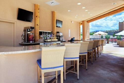 A modern outdoor bar with high stools, a counter, and TVs, surrounded by umbrellas and a scenic view.