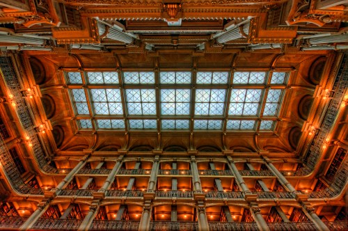 A grand library interior with ornate architecture, featuring a glass ceiling and multiple levels of bookshelves.