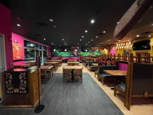 Interior of a vibrant restaurant with colorful murals, empty tables, and chairs stacked on tables.