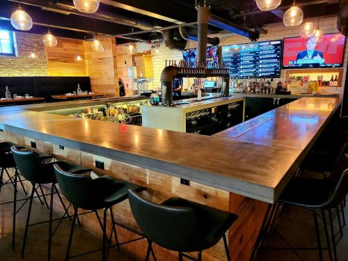A modern bar with a concrete countertop, wooden accents, and a variety of drinks displayed behind the counter.