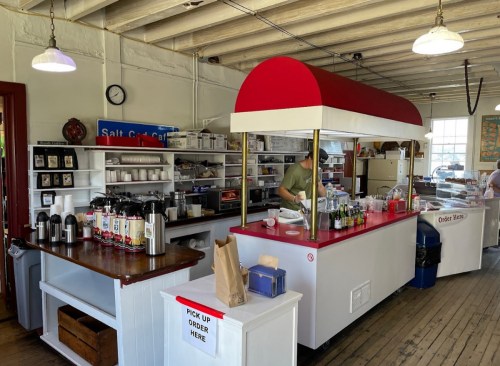 A cozy café interior with a red and white counter, shelves of supplies, and a sign indicating where to order.