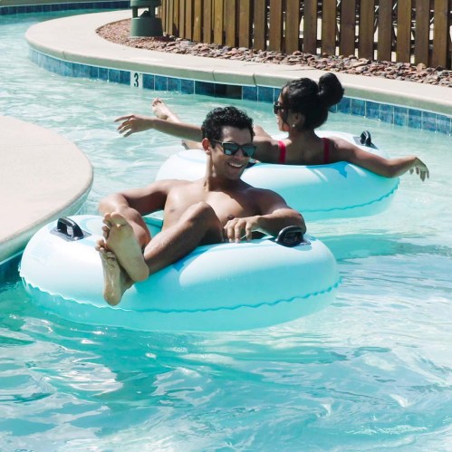 Two people relax on inner tubes in a pool, enjoying a sunny day. One is wearing sunglasses and smiling.