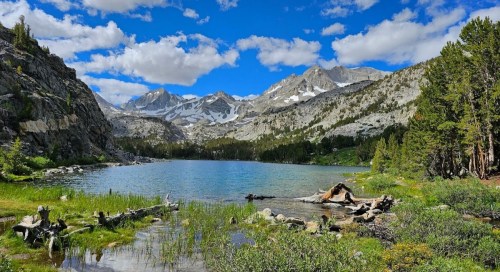 A serene mountain lake surrounded by lush greenery and towering peaks under a blue sky with fluffy clouds.