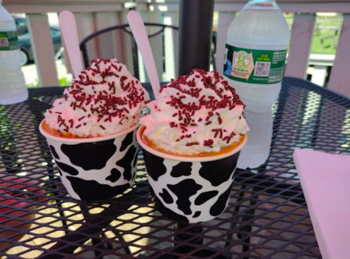 Two cups of ice cream topped with whipped cream and red sprinkles, sitting on a table next to a water bottle.
