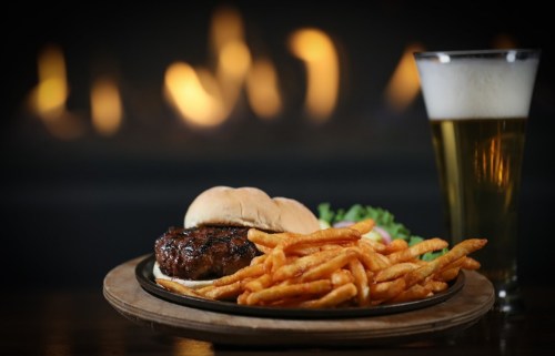 A juicy burger with fries and a side of lettuce, accompanied by a glass of beer, set against a warm, glowing background.