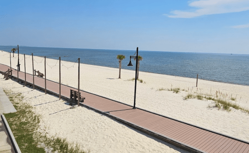 A serene beach scene with a wooden walkway, palm trees, and calm blue waters under a clear sky.