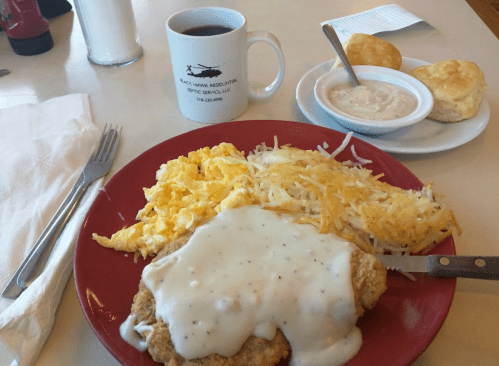 A plate of chicken fried steak with gravy, scrambled eggs, hash browns, biscuits, and a cup of coffee.