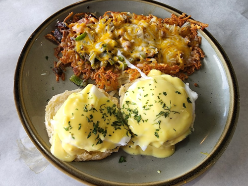 A plate with two eggs Benedict topped with hollandaise sauce and a side of cheesy hash browns.