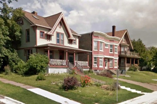 Three distinct houses with porches and gardens, set against a cloudy sky. Greenery and flowers line the front yards.