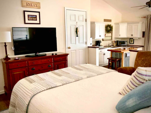 Cozy bedroom with a large TV, kitchen area, and a relaxing atmosphere, featuring a bed with a striped throw pillow.