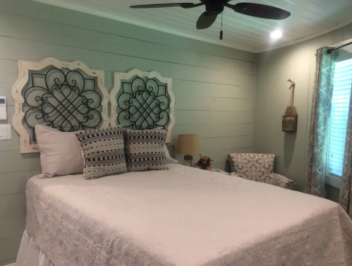 Cozy bedroom with a large bed, decorative headboard, patterned pillows, and a chair by a window.