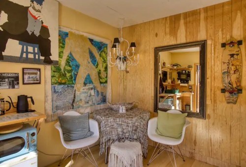 Cozy interior with wooden walls, a chandelier, art pieces, and a small dining area featuring two chairs and a table.