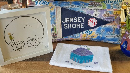 A framed quote, a decorative pillow with "Jersey Shore," and a towel featuring a cake illustration, all showcasing New Jersey themes.