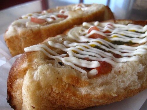 Close-up of two toasted bread halves topped with mayonnaise, chopped tomatoes, and green chutney.