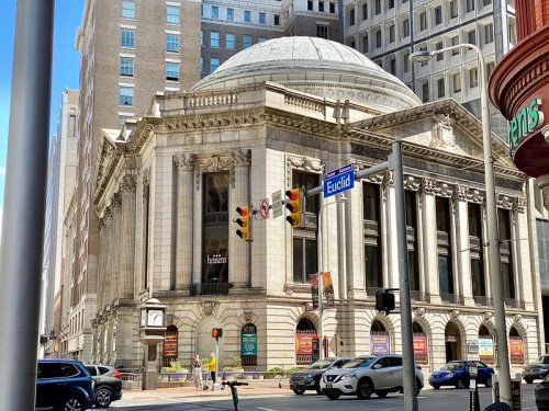 Historic building with a dome, located at a busy intersection, surrounded by modern skyscrapers and traffic.