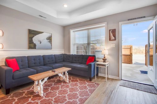 Cozy living room with a blue sectional sofa, wooden coffee table, and natural light from a door leading outside.