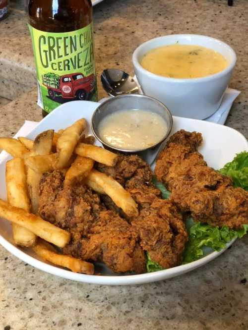 A plate of fried chicken with fries, served with a bowl of soup and a bottle of Green Chili Cerveza.