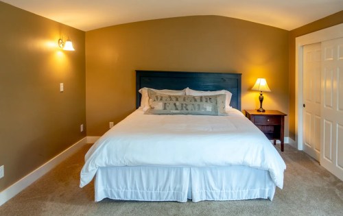 Cozy bedroom with a large bed, decorative pillow, nightstand, and warm wall colors. Soft lighting creates a welcoming atmosphere.