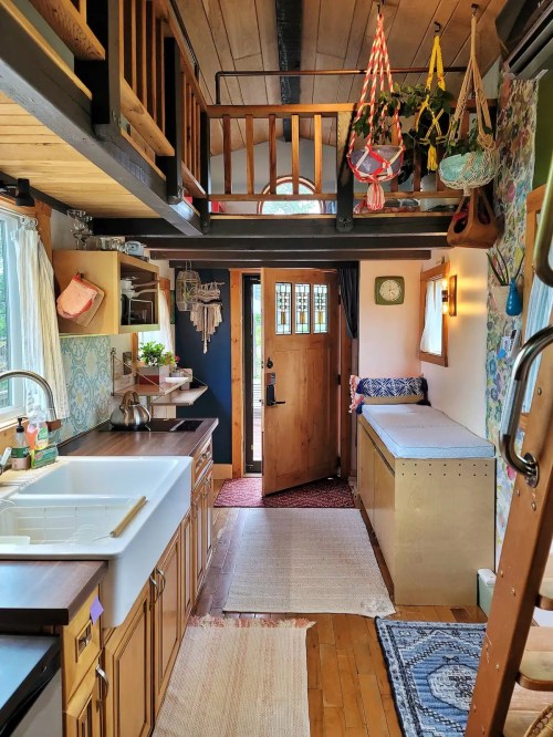 Cozy tiny home interior with a kitchen, seating area, and lofted space, featuring wooden accents and colorful decor.