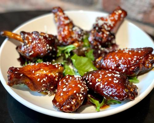 A plate of glazed chicken wings garnished with sesame seeds and served on a bed of greens.