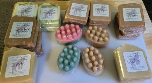 A variety of handmade soaps in different shapes and colors, each labeled with their scent, arranged on a white surface.