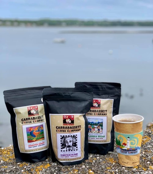 Three bags of Carrabassett Coffee Company coffee and a coffee cup sit on a stone ledge with a scenic background.