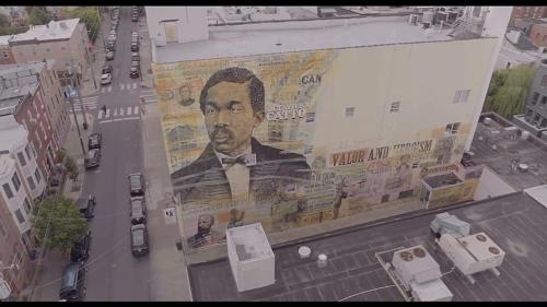 Aerial view of a mural depicting a historical figure, with the words "Valor and Heroism" on a building's exterior.