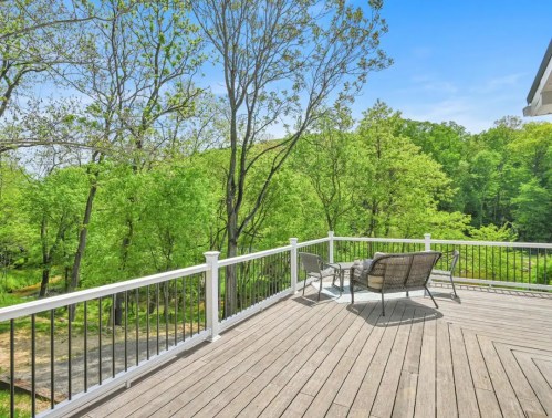 A spacious deck with seating overlooks a lush green landscape and trees under a clear blue sky.