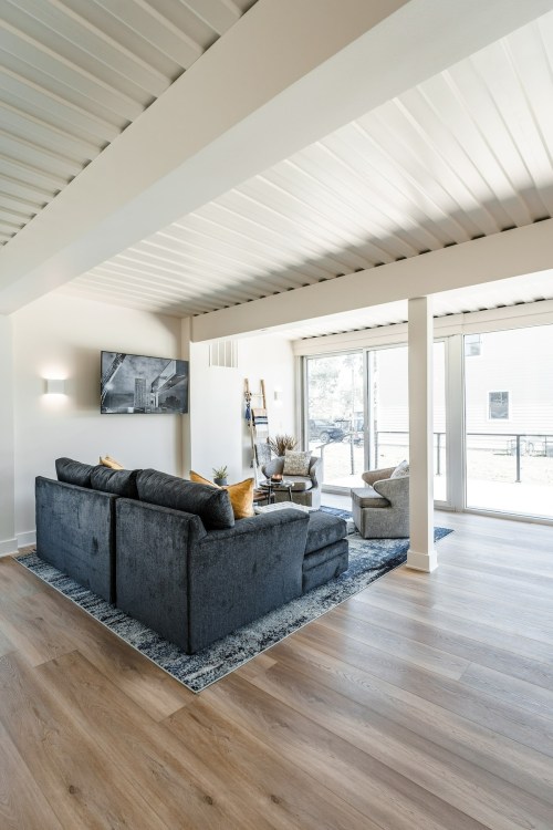 Modern living room with a gray sofa, armchair, TV, and large windows letting in natural light.