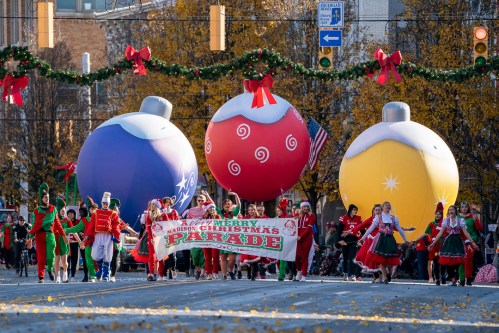 A festive parade featuring large Christmas ornaments and performers in holiday costumes, celebrating the season.